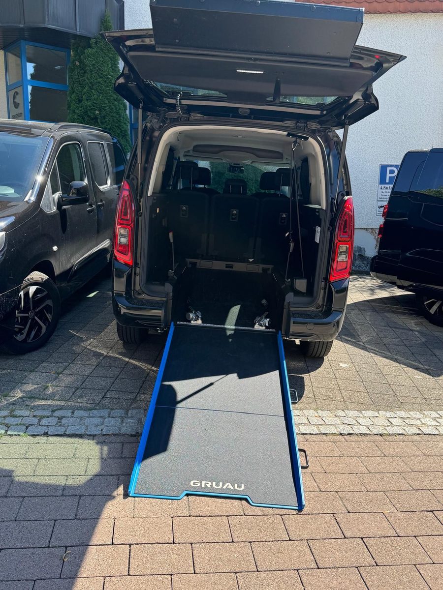 Heck eines schwarzen Toyota Proace City mit geöffneter Heckklappe und ausgefahrener Rollstuhlrampe, dahinter Rückhaltegurte im Laderaum
